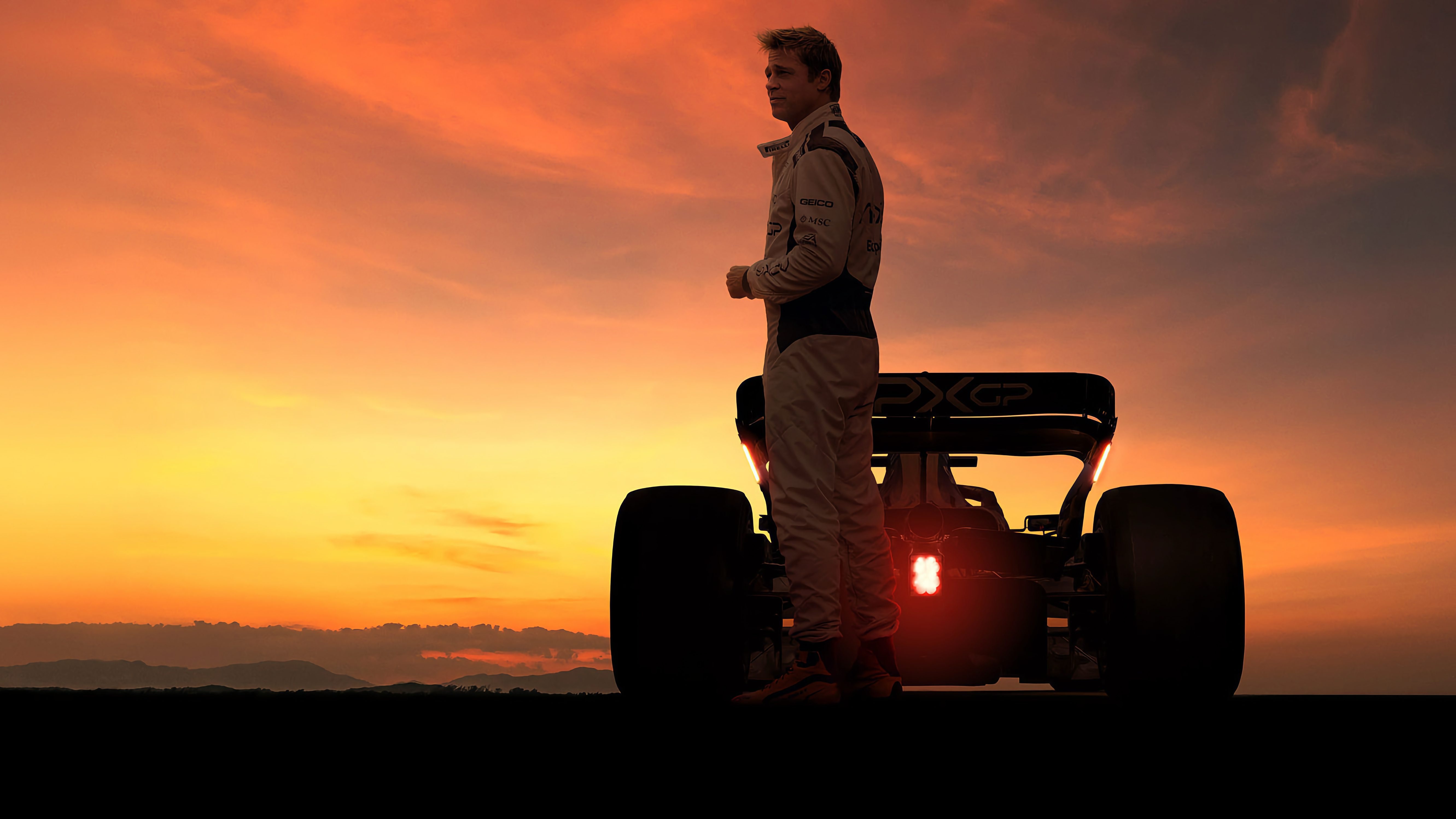 Ein Rennfahrer in einem hellen Rennanzug steht neben einem Formel-1-Rennwagen bei Sonnenuntergang, der Himmel ist orange und rot gefärbt.