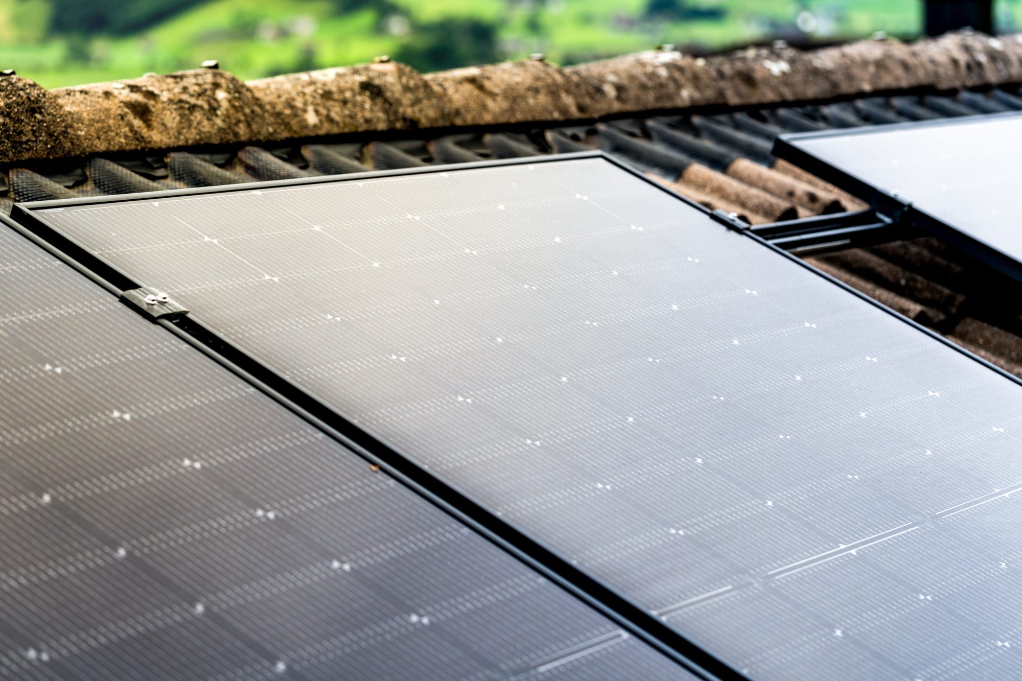 Solarmodule auf einem Dach mit Ziegeln, im Hintergrund unscharfe grüne Landschaft.