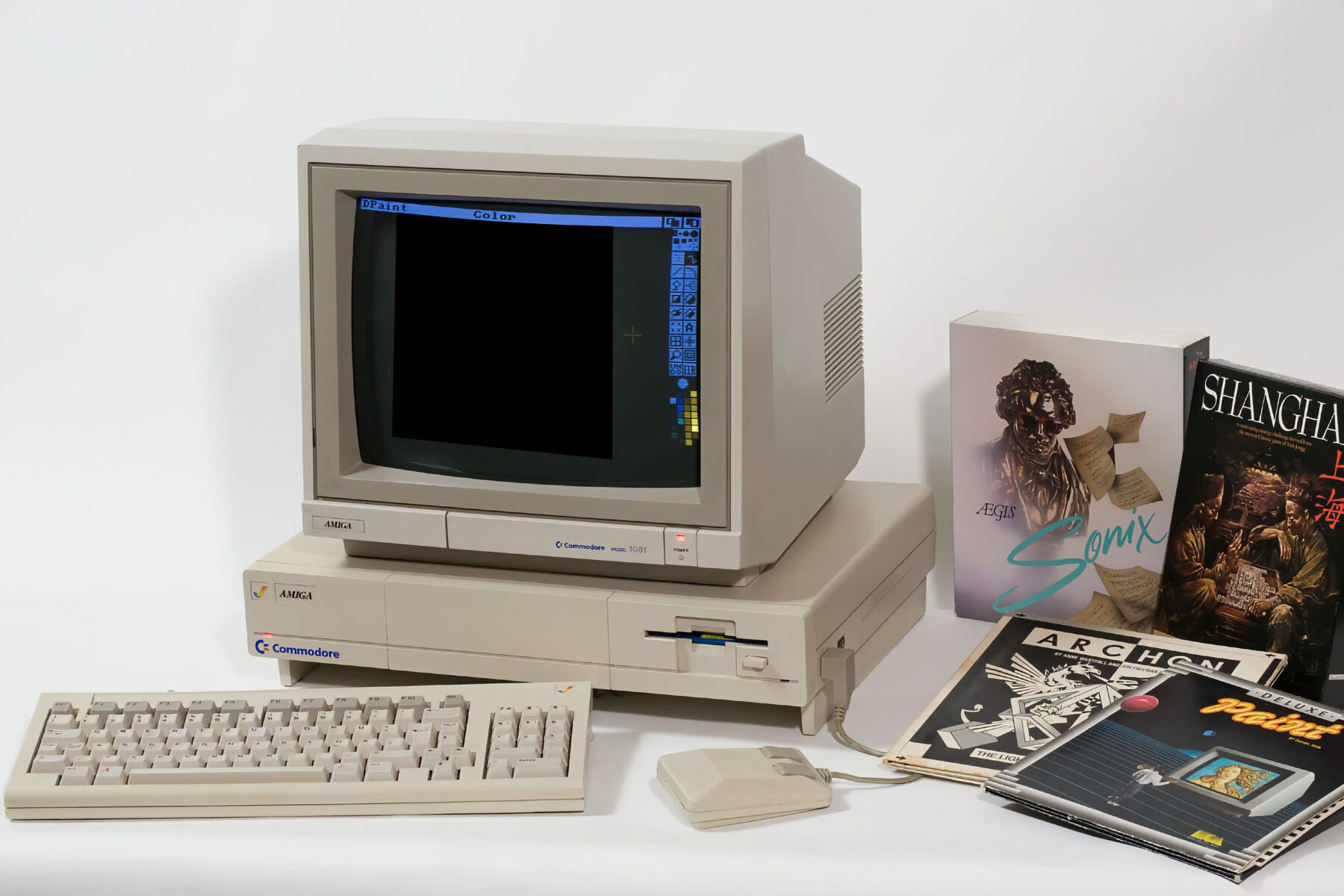 Commodore Amiga 1081 Monitor auf einem beigefarbenen Commodore Amiga Computer mit Tastatur und Maus, daneben mehrere Spiele- und Softwareverpackungen und Handbücher. Der Monitor zeigt ein geöffnetes Malprogramm namens "DPaint".