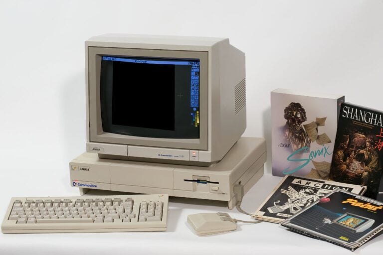 Commodore Amiga 1081 Monitor auf einem beigefarbenen Commodore Amiga Computer mit Tastatur und Maus, daneben mehrere Spiele- und Softwareverpackungen und Handbücher. Der Monitor zeigt ein geöffnetes Malprogramm namens "DPaint".