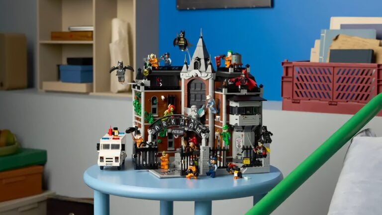 LEGO-Modell des Arkham Asylum mit mehreren Batman- und Joker-Figuren, auf einem blauen runden Tisch in einem Raum mit Regalen und Kisten im Hintergrund.